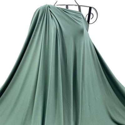Moss Green bamboo knit fabric draped on a hanger against a white background - Fabric Collection