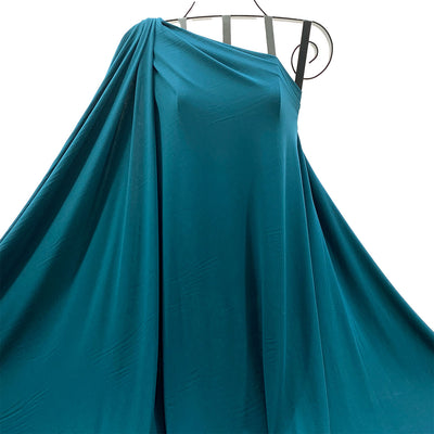 Petrol blue bamboo knit fabric draped one-shoulder dress on a hanger against a white background - Fabric Collection